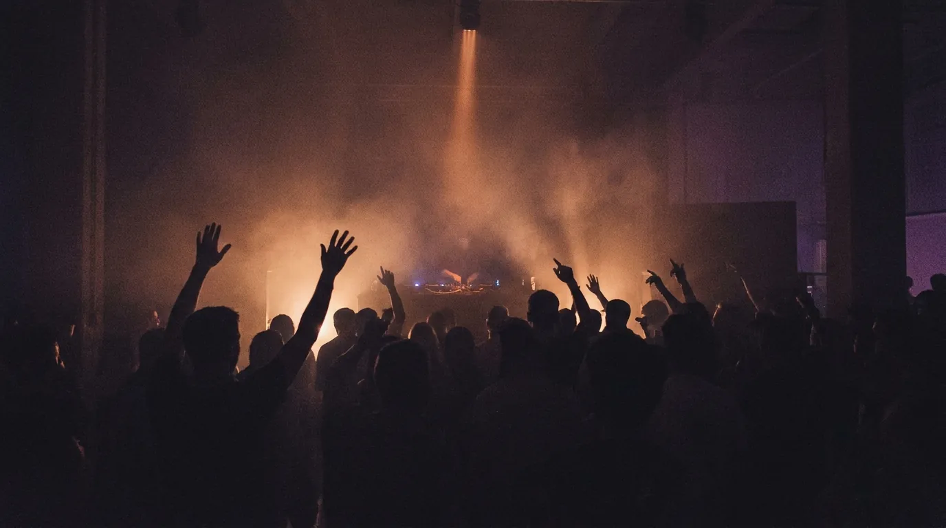 A 4AM melodic techno club at peak hour, silhouetted crowd raising hands into copper-lit fog