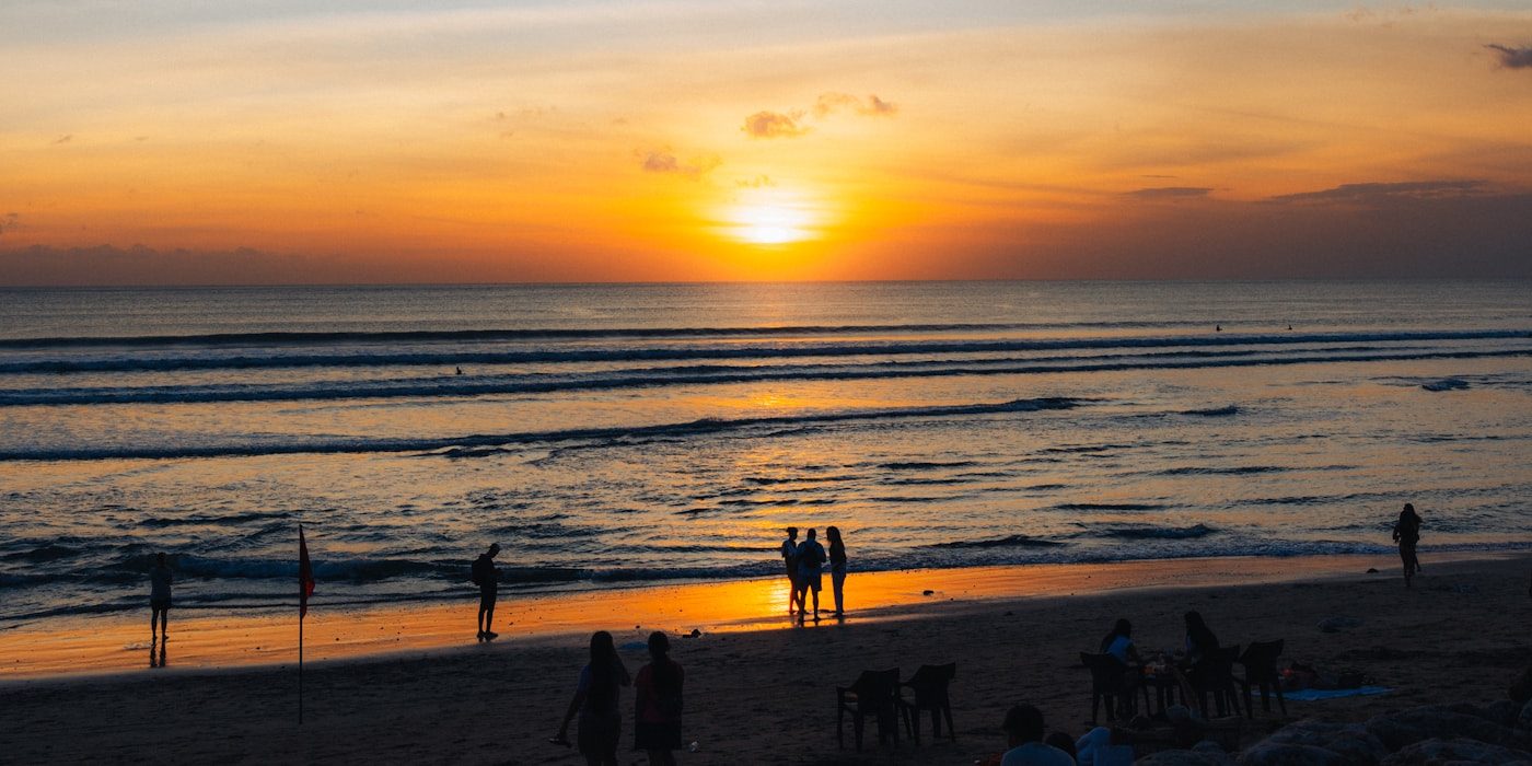 Friends gathered on a tropical beach at sunset in Bali, Indonesia — the golden-hour format Asia-curated afro house playlists program against